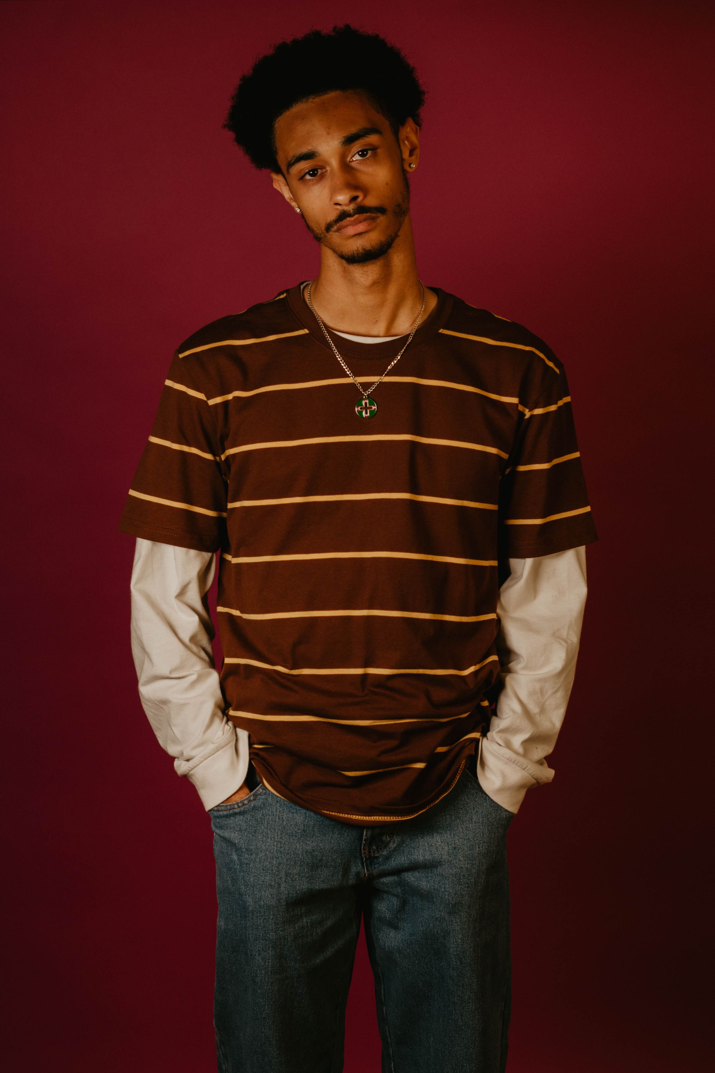 Full length fashion portrait of model in striped sweater and jeans against red wall.