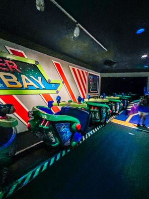 A row of neon-lit laser tag vehicles in green and blue against a colorful graffiti wall in a dark arcade setting.