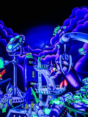Neon-lit futuristic amusement park scene with glowing blue and green mechanical structures against dark cloudy background.