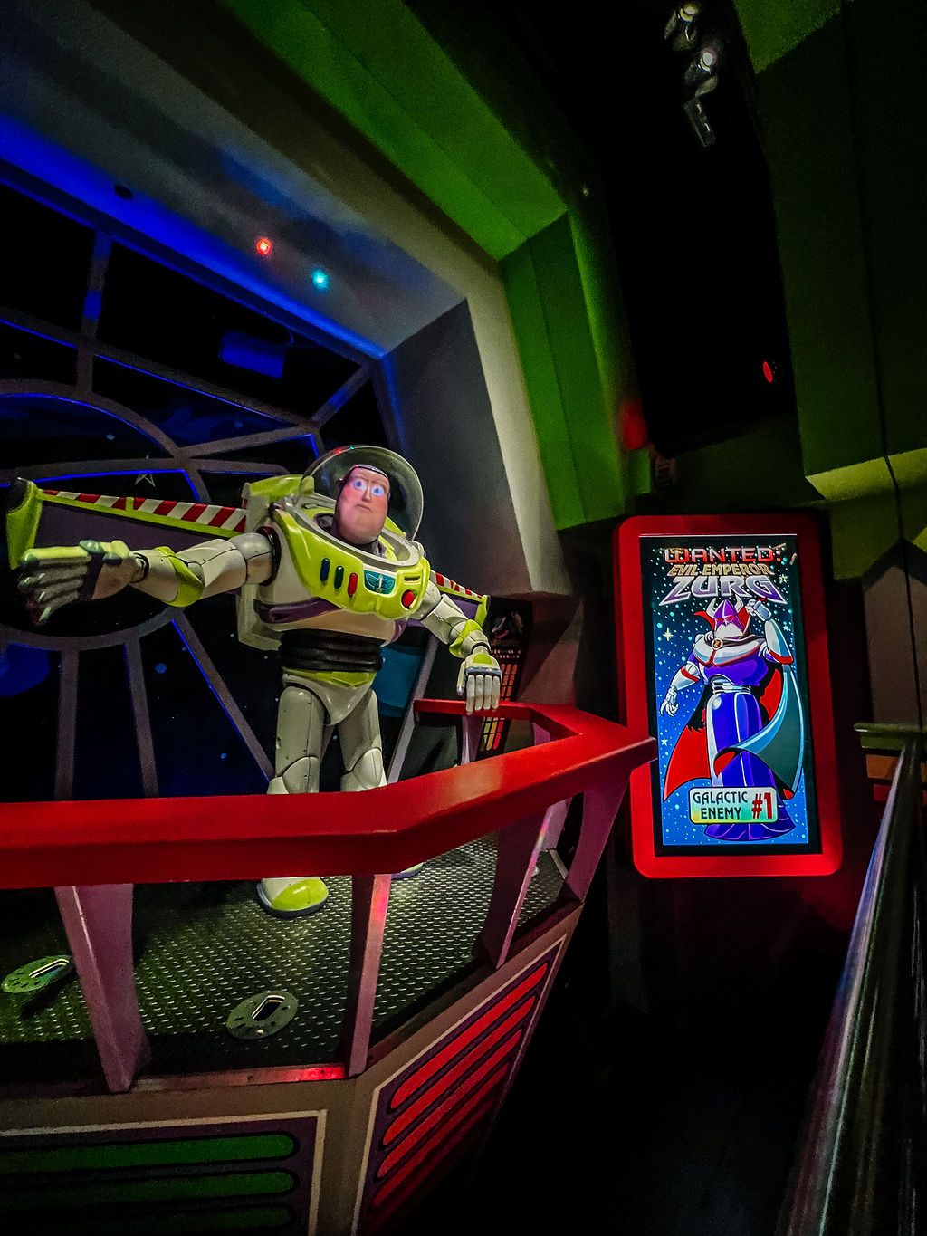 Buzz Lightyear animatronic figure and digital display panel with neon lighting effects at a Disney theme park attraction.
