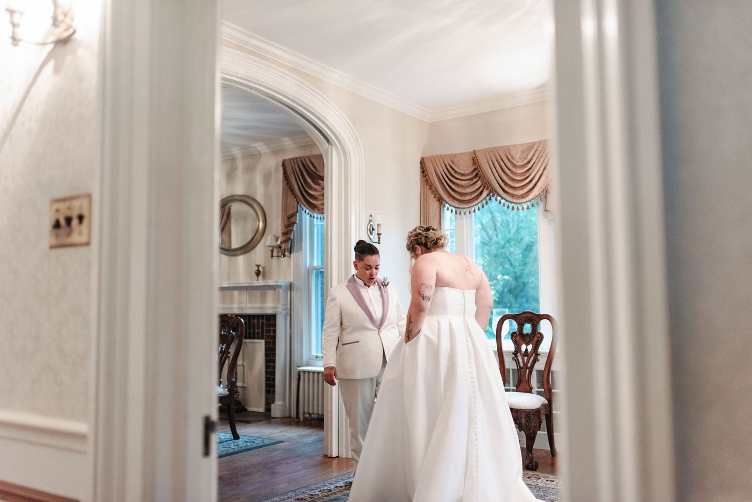 A couple shares an intimate moment in a grand room with white walls and elegant drapes.