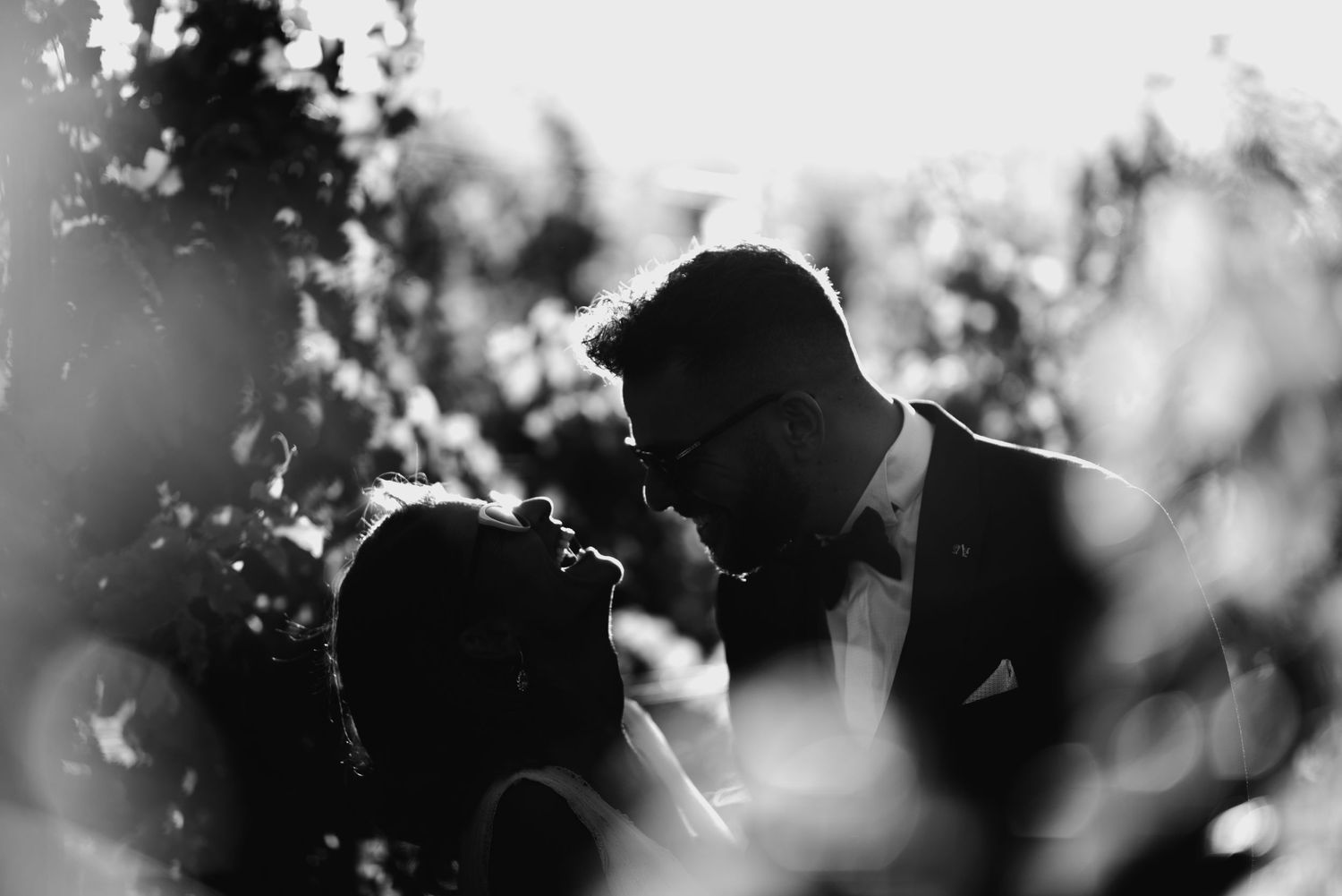 An artistic black and white photo of a couple sharing an intimate moment through foliage.