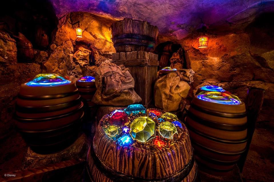 Colorful illuminated water features and glowing elements create a magical display inside a dimly lit cave environment.