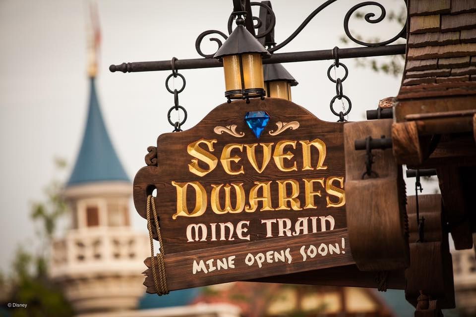 Rustic wooden signs for Seven Dwarfs Mine Train attraction hanging from metal chains at Disney theme park.