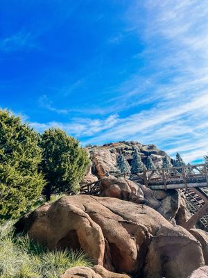 A panoramic view of rugged desert rock formations under vibrant blue skies with white wispy clouds.