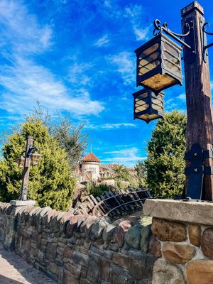 Ornate black lanterns hang on a stone wall with a blue sky and castle-like building in the background at Disney World.