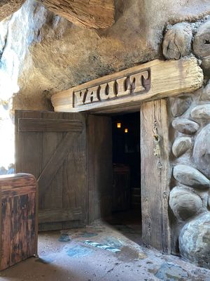 Rough-hewn wooden doors and rocky cave walls form a tunnel-like passageway in an ancient stone structure.