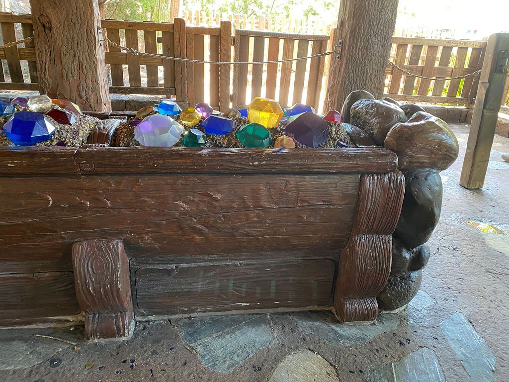Decorative round wood logs line a rustic backyard fence with various toys and items scattered along the base of it.