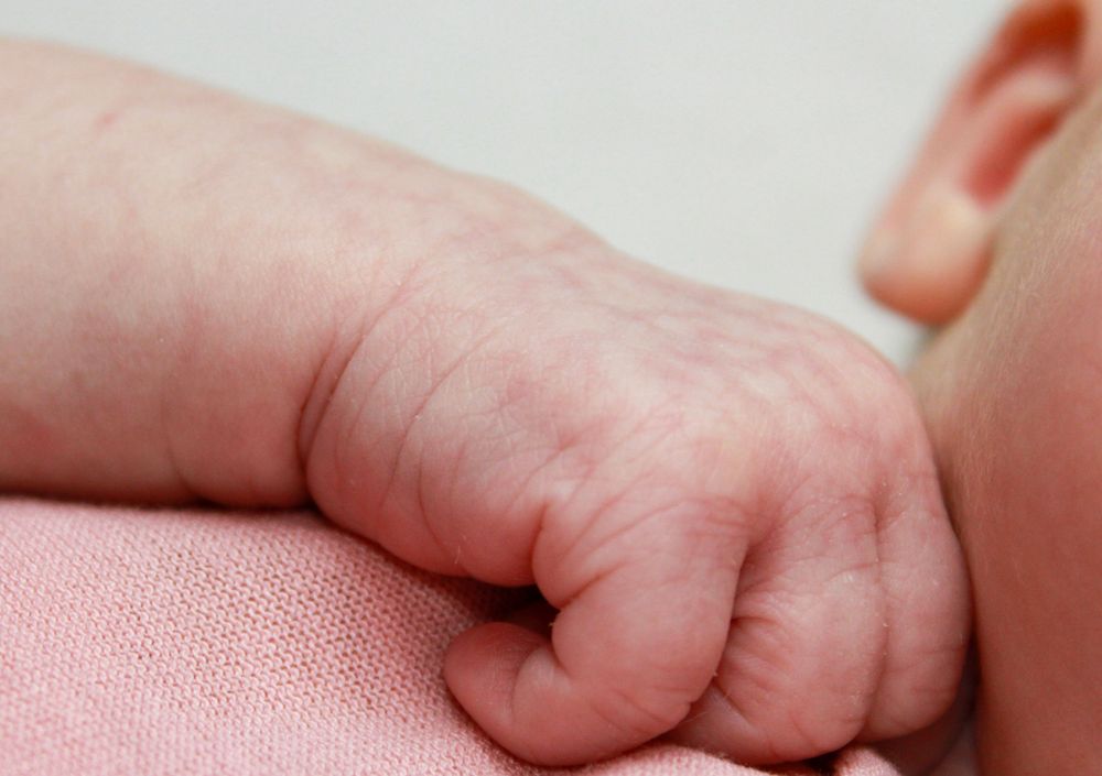 Close-up photograph of a newborn baby's tiny hand against pink fabric.