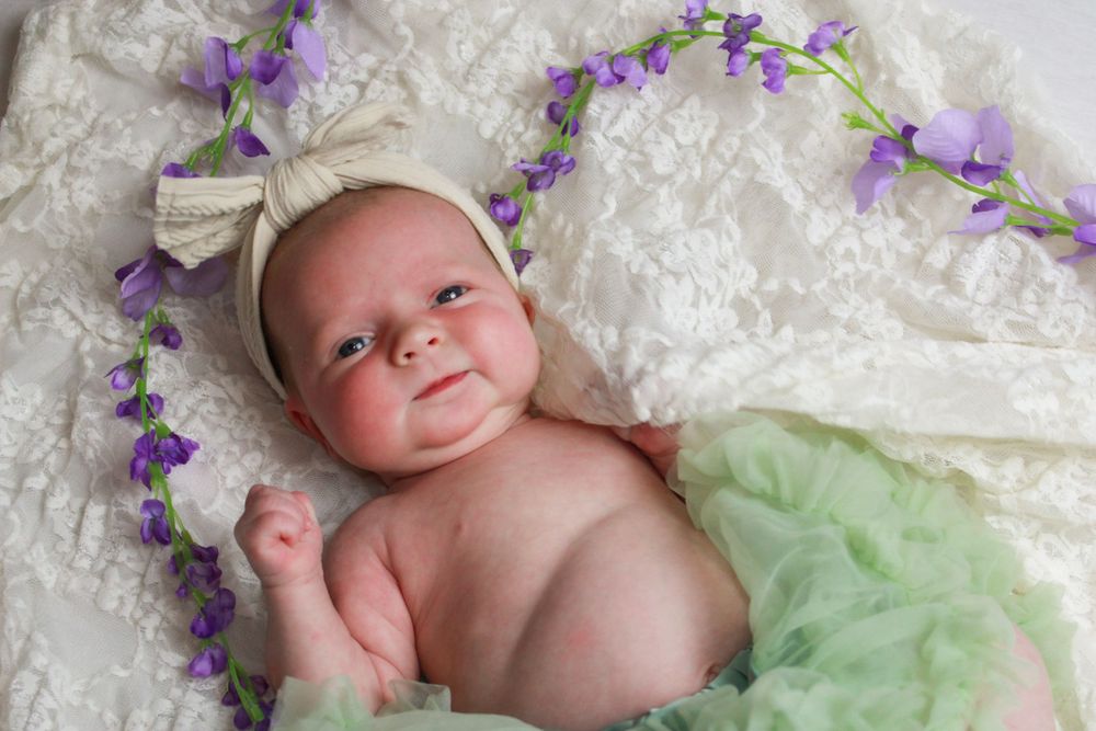 Newborn portrait with purple flowers and white lace featuring delicate styling.
