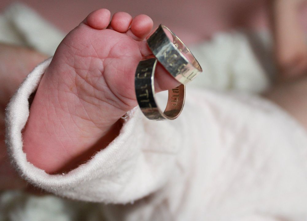 Wedding rings balanced on tiny infant foot wrapped in white fabric.