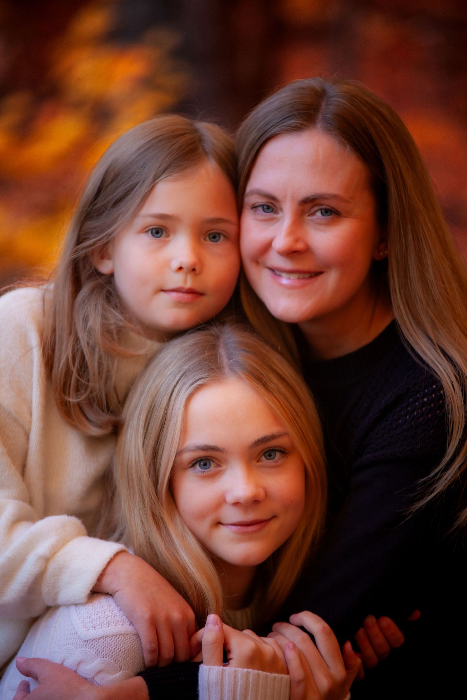 Close-up of mom, big sis, and little sis enjoying a cozy moment outdoors, surrounded by the rich colors of autumn leaves.