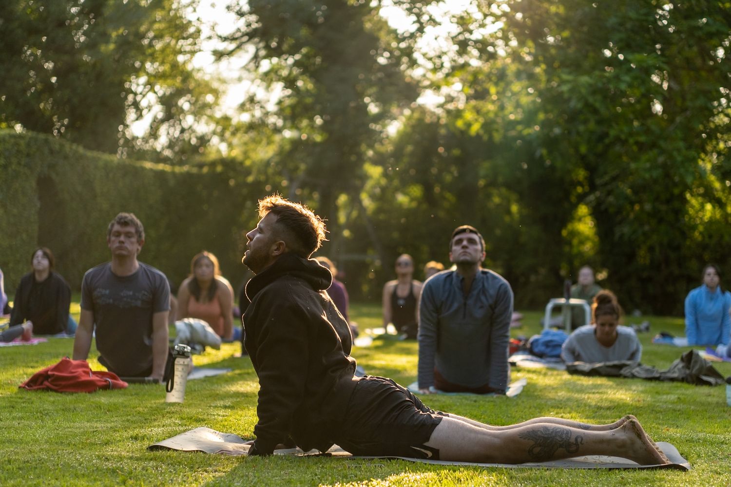 Group practicing yoga outdoors on mats during sunset in park setting.