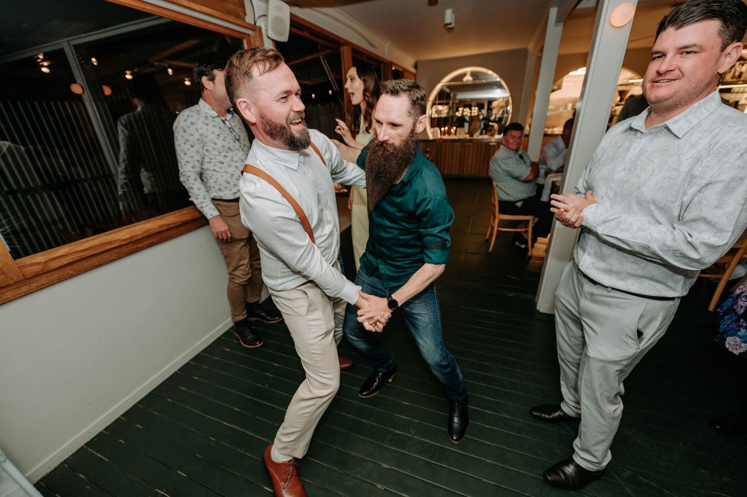 Wedding guests dancing and celebrating on indoor dance floor during reception.