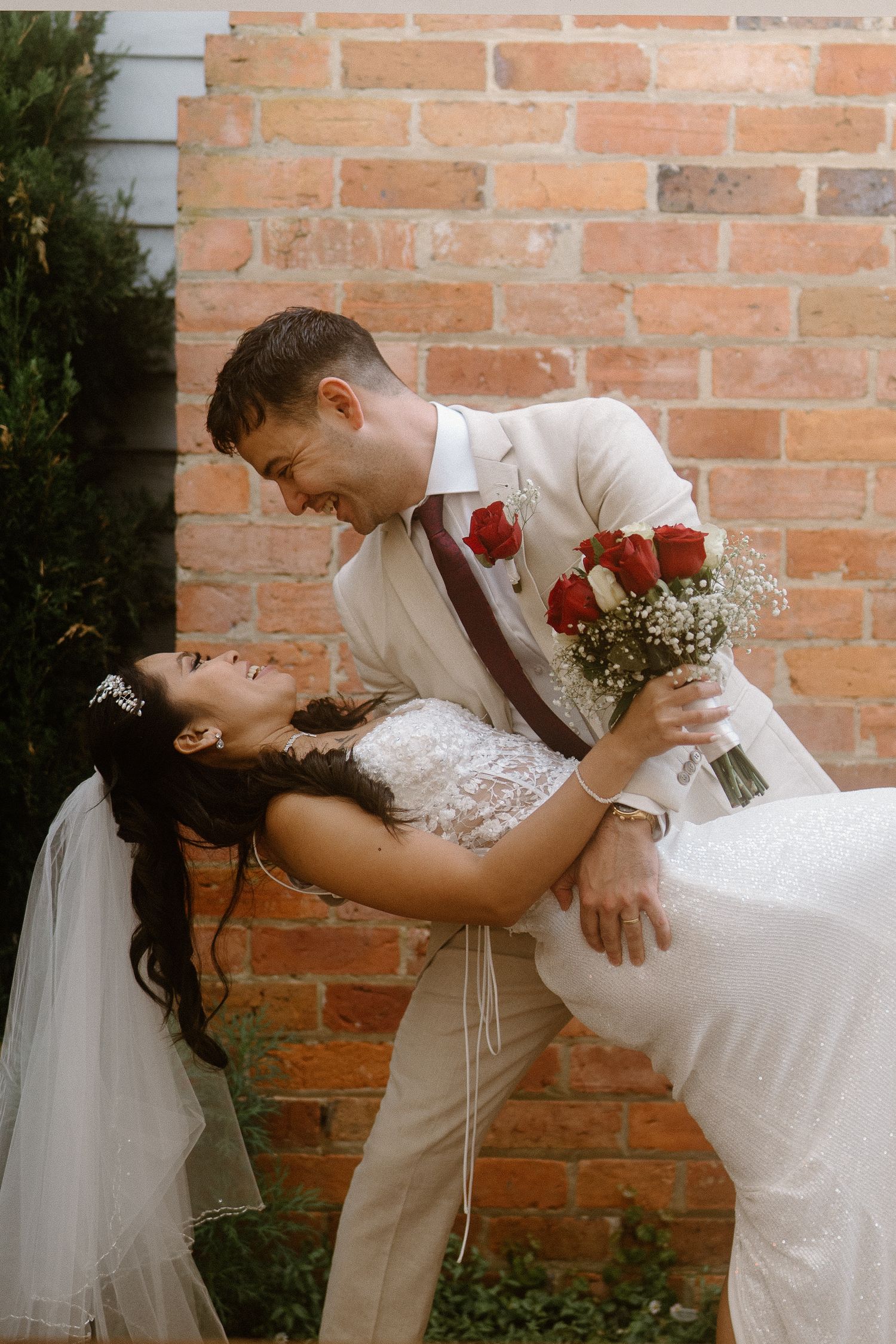 Newlyweds sharing a dip pose against a brick wall with red roses in the bouquet. Stellina Restaurant, Traralgon, Gippsland, Victoria.
