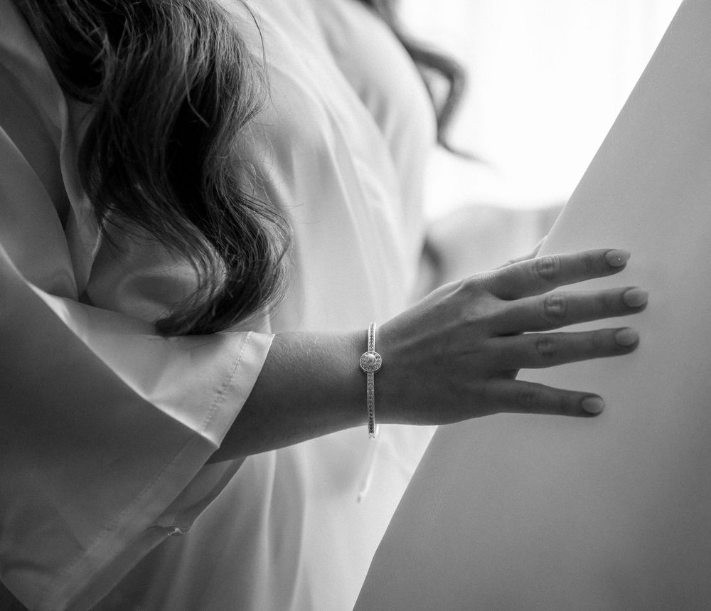 Close-up of a delicate hand wearing an elegant bracelet against a white robe in soft lighting.