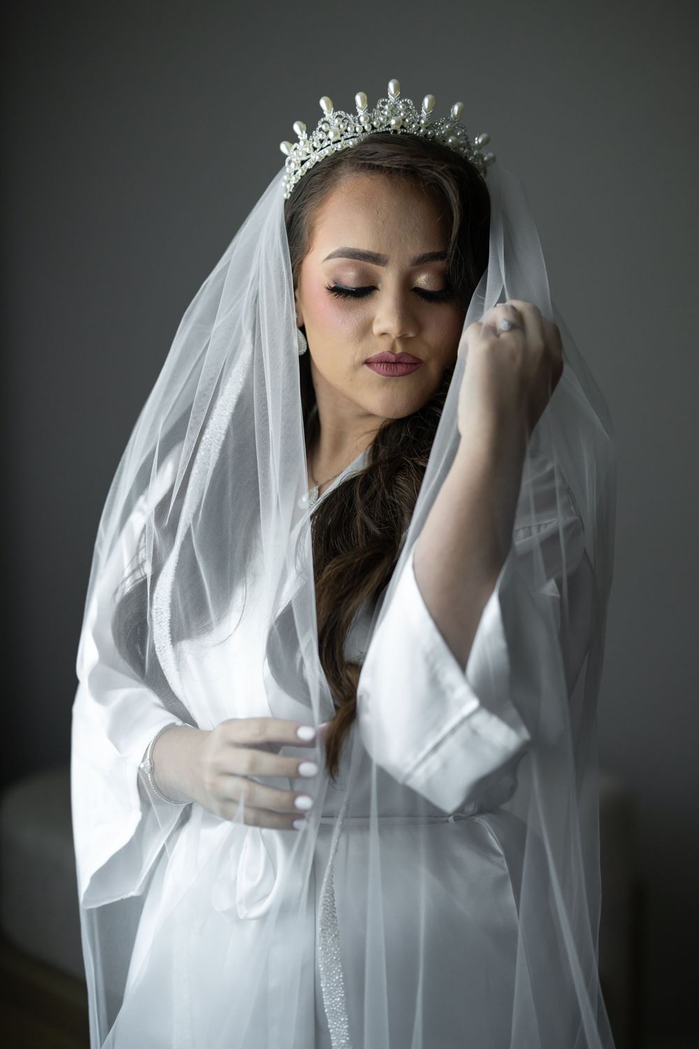 Ethereal bridal portrait with flowing veil and crystal crown against dark background.