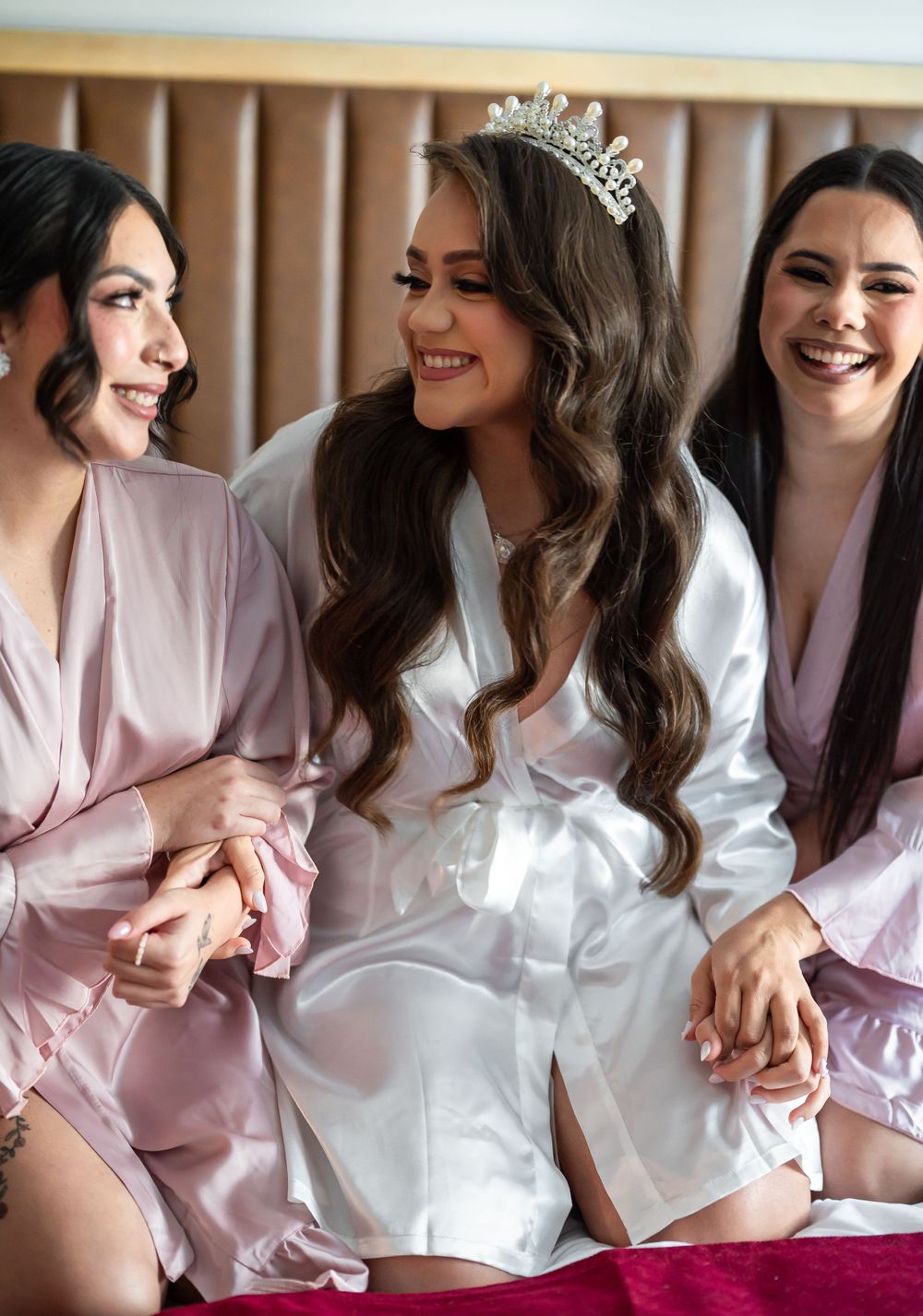 Three friends in silk robes share joyful laughter during pre-wedding preparations.