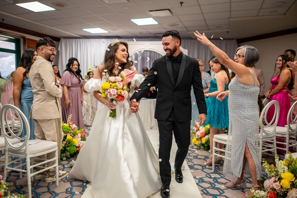 A newlywed couple exits their ceremony while guests celebrate with yellow floral decorations.