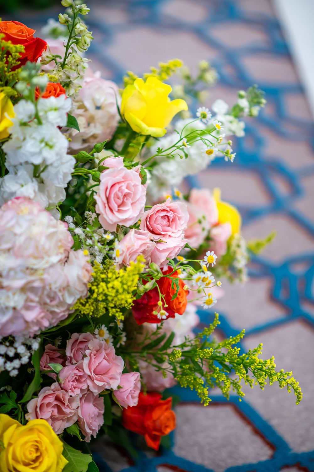 Colorful wedding floral arrangement with pink roses, yellow and red blooms on blue surface.