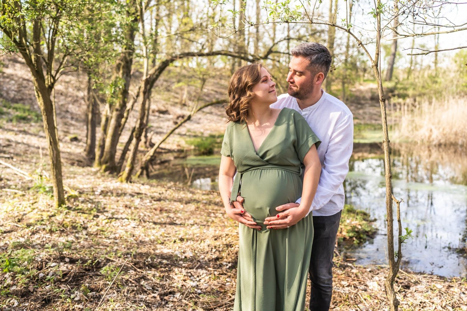 Tender maternity moment captured in natural woodland setting with couple by water.