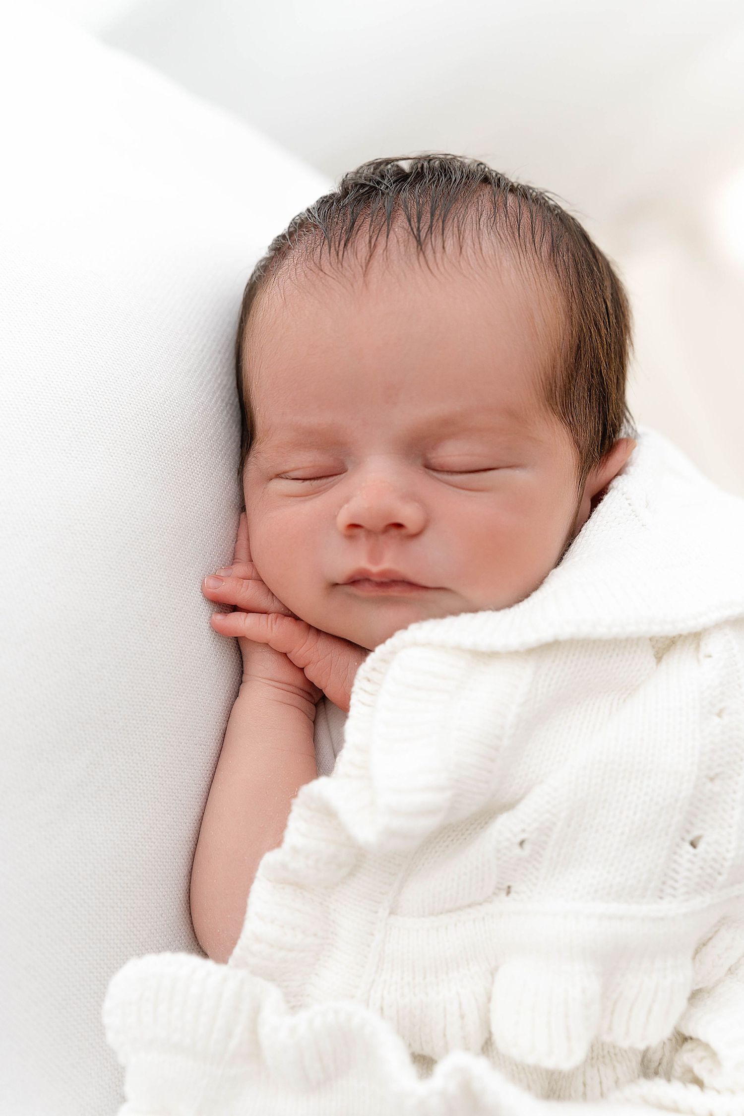 Close-up of sleeping newborn baby with dark hair against white background.
