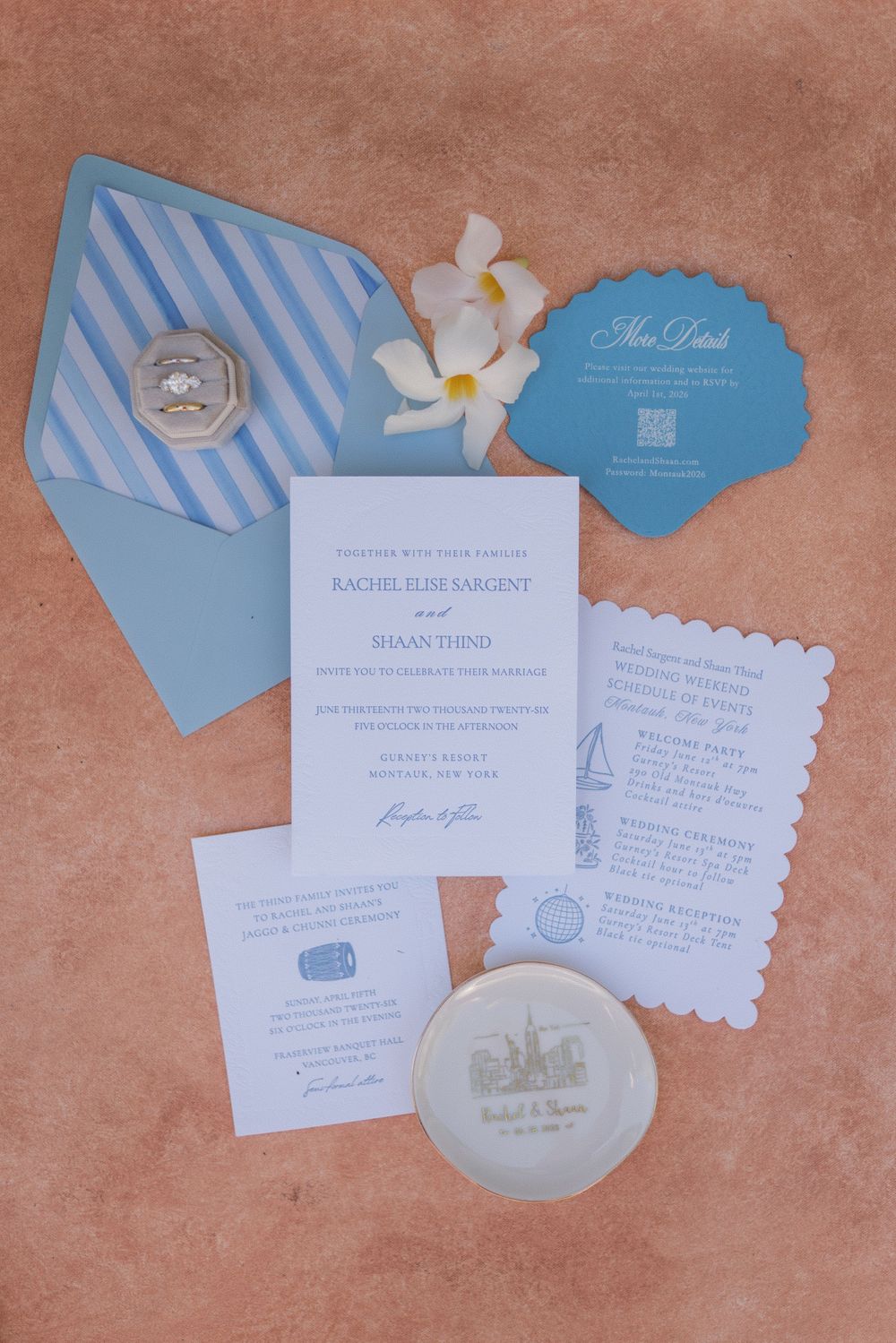 Blue and white wedding invitation suite with striped envelope, shell details, and floral accents on terracotta background.