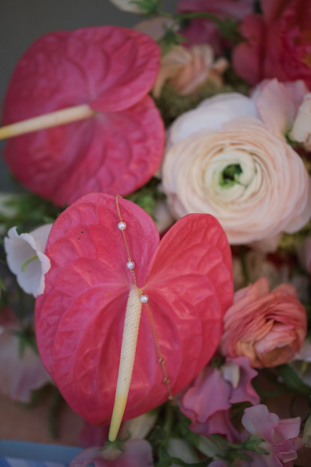 Close-up of vibrant red anthurium flowers with pearl accents among soft pink ranunculus blooms.