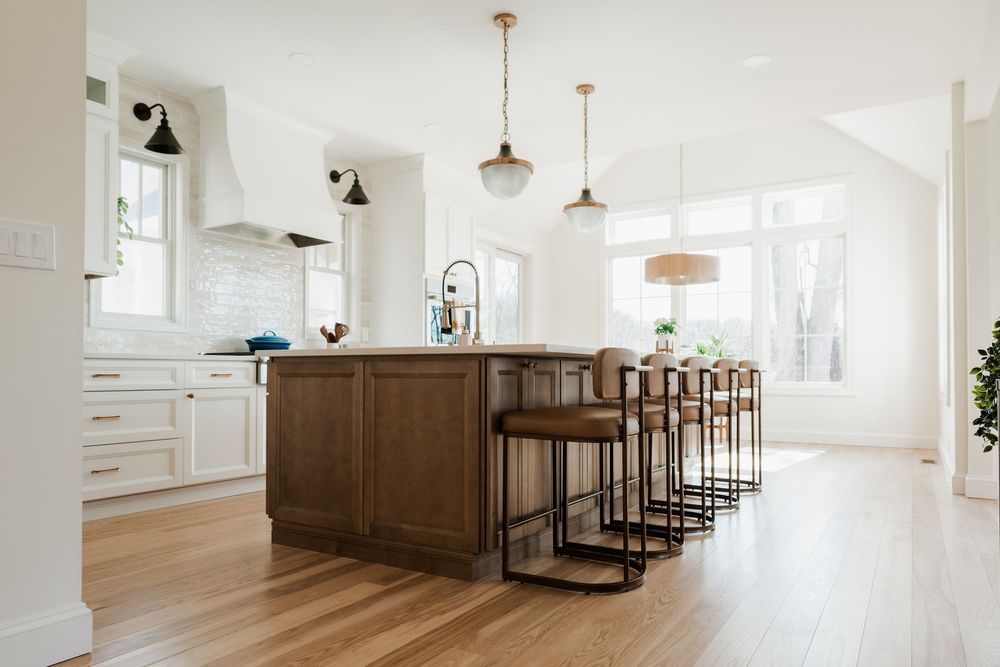 Modern kitchen with white cabinets, dark wood island, bar stools, pendant lights, and hardwood floors.