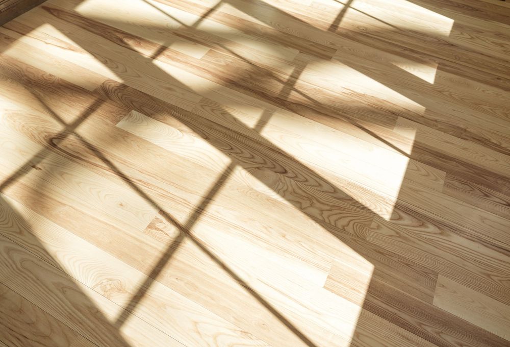 Sunlight casting geometric shadows on smooth light oak hardwood flooring planks in a bright interior room.