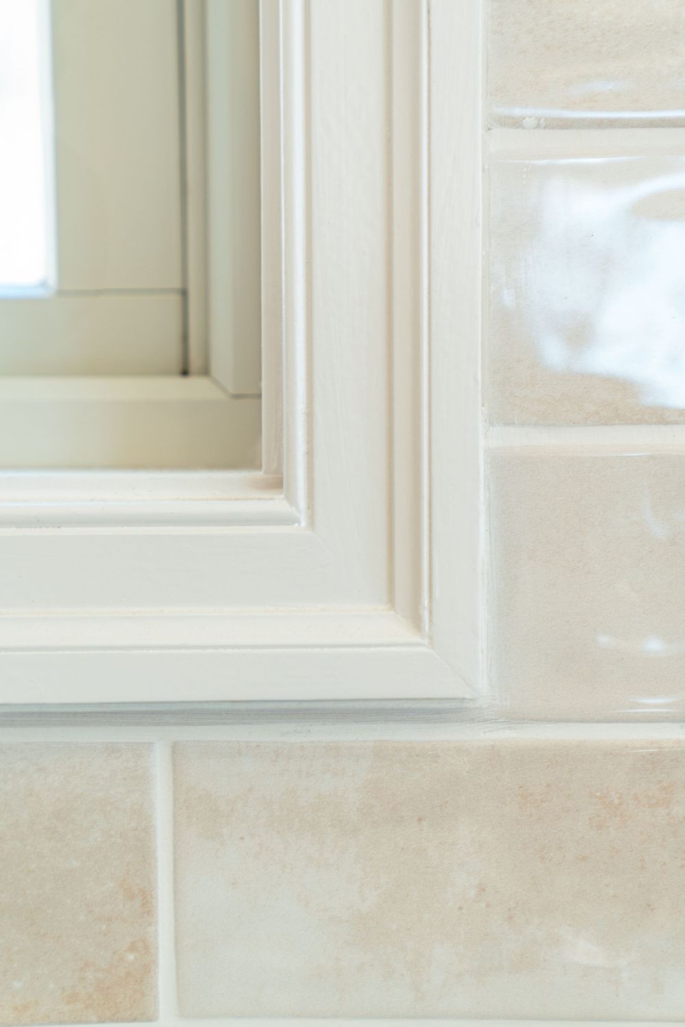 Close-up of a white framed mirror above beige ceramic subway tiles in a bright bathroom.