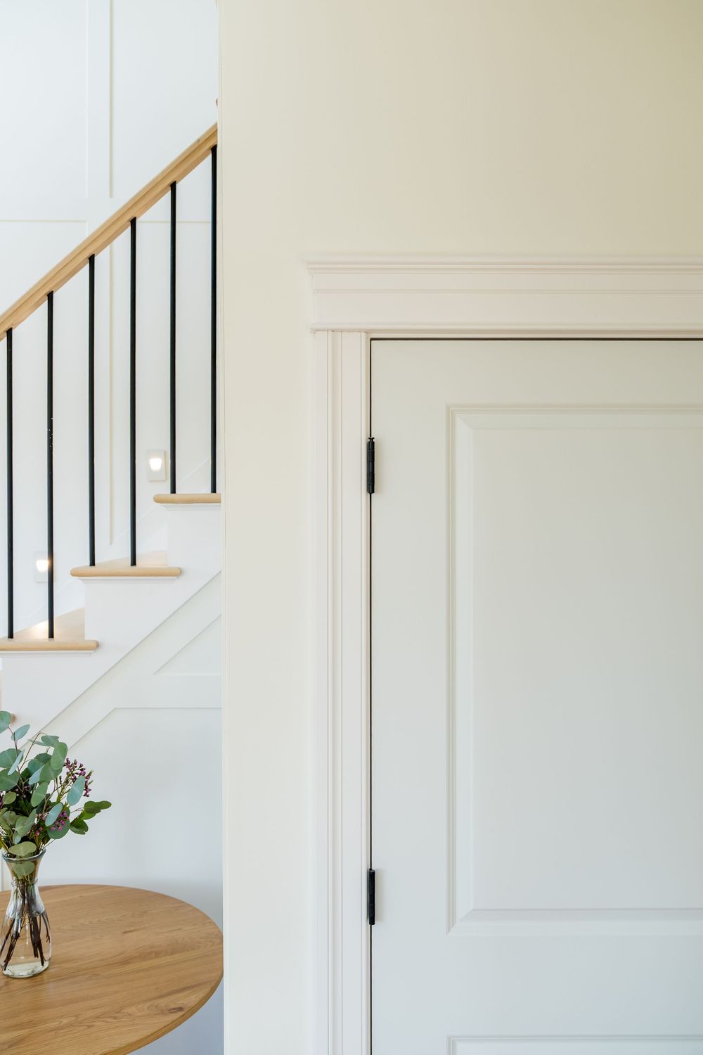 Elegant home entryway featuring white paneled doors, modern staircase with black metal balusters, and a round wood table.