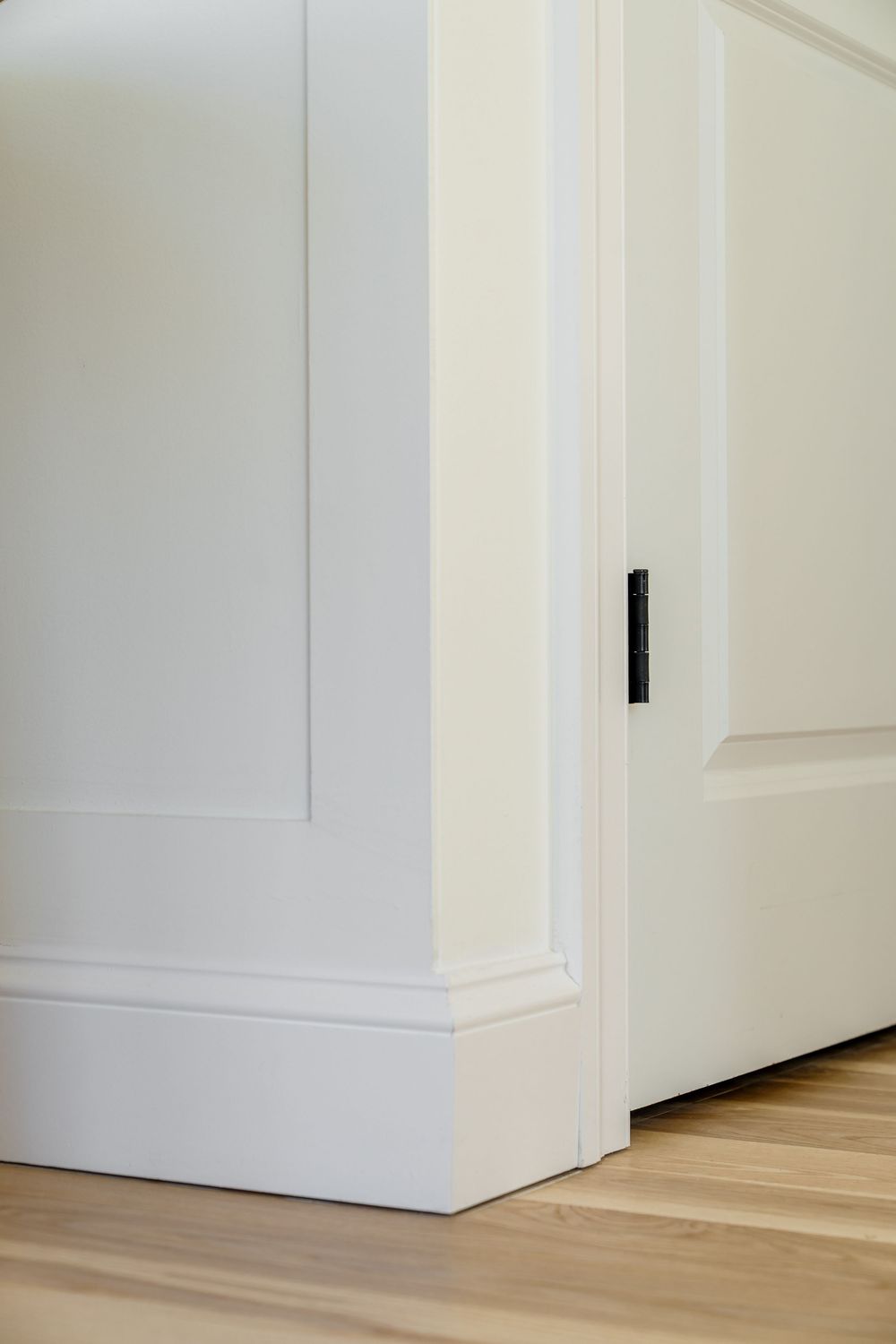 White paneled wall with black hardware sliding door and light hardwood floor.