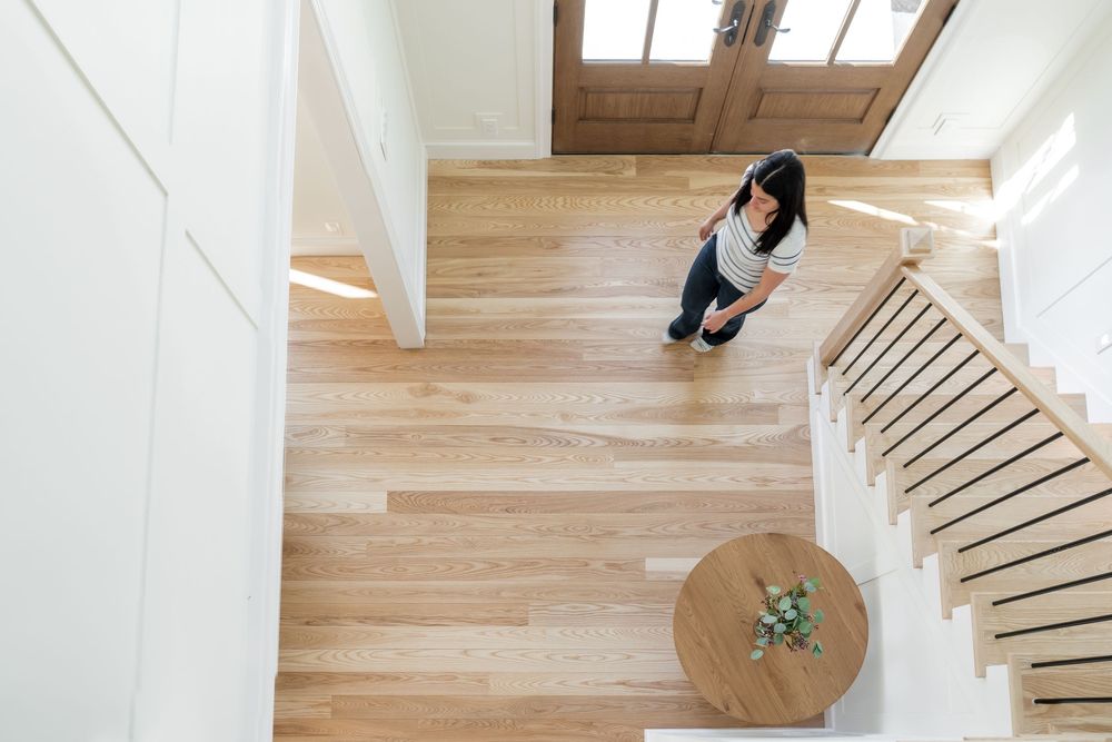 Aerial view of a woman standing on light hardwood floors in a modern home entryway with white staircase.