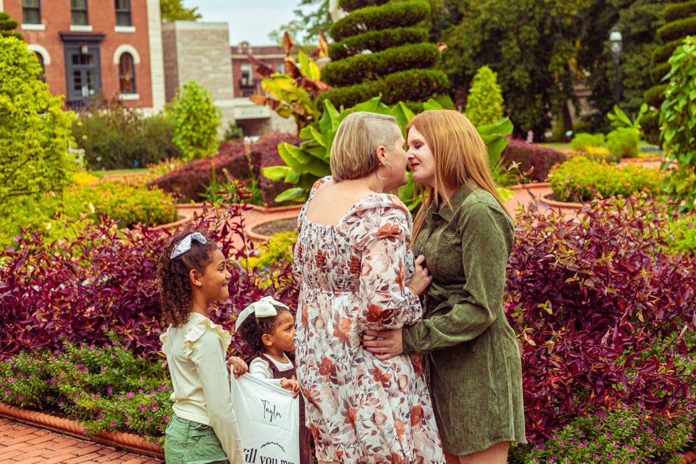 Family of four posing in a colorful garden with lush red and green foliage in the background.
