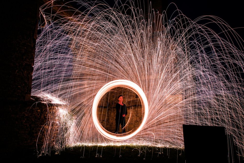 Person spinning glowing steel wool in a circle creating dramatic orange sparks against a dark night sky.