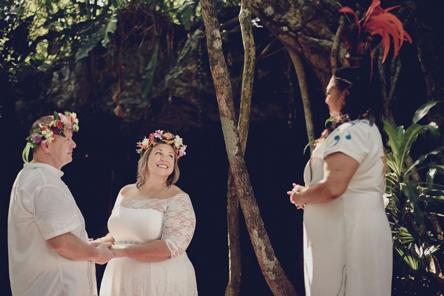 Bride and groom in white attire and floral crowns participate in an outdoor mayan wedding ceremony under tropical foliage.