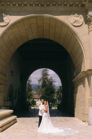 Bride and groom embracing under grand stone arch at elegant wedding venue with mountain views.