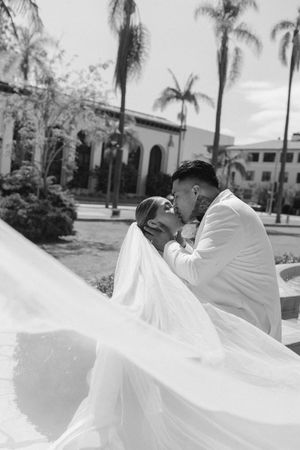 Black and white photo of a bride and groom sharing a romantic kiss as her veil billows in the breeze.
