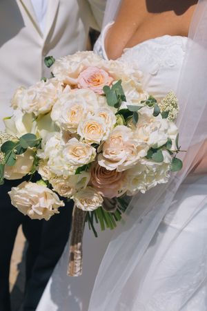 Close-up of elegant bridal bouquet featuring cream and blush roses, peonies, and eucalyptus greenery held by bride.