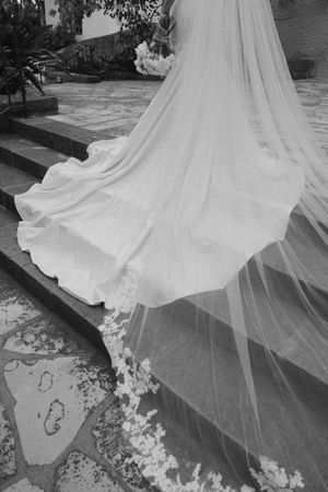 Black and white photo of a bride's flowing wedding gown and veil trailing on stone steps.