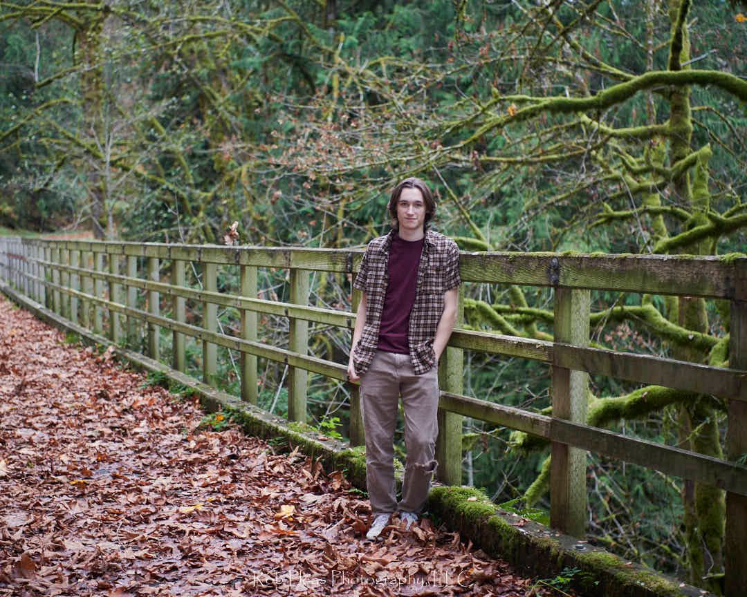High school senior male at Snoqualmie-Preston trail standing but leaning against old wooden fence along old train rail to trail.