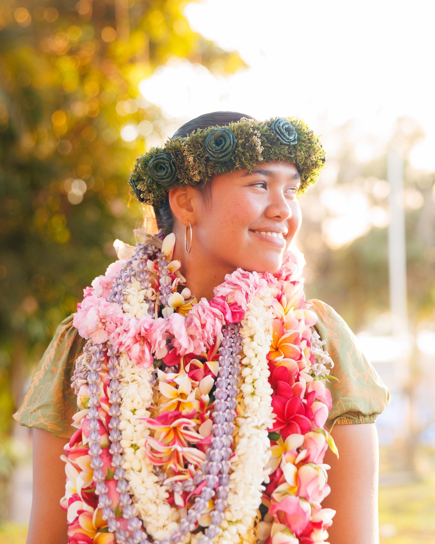 Young woman smiles beautifully wearing colorful floral leis and a green flower crown in Hawaii.