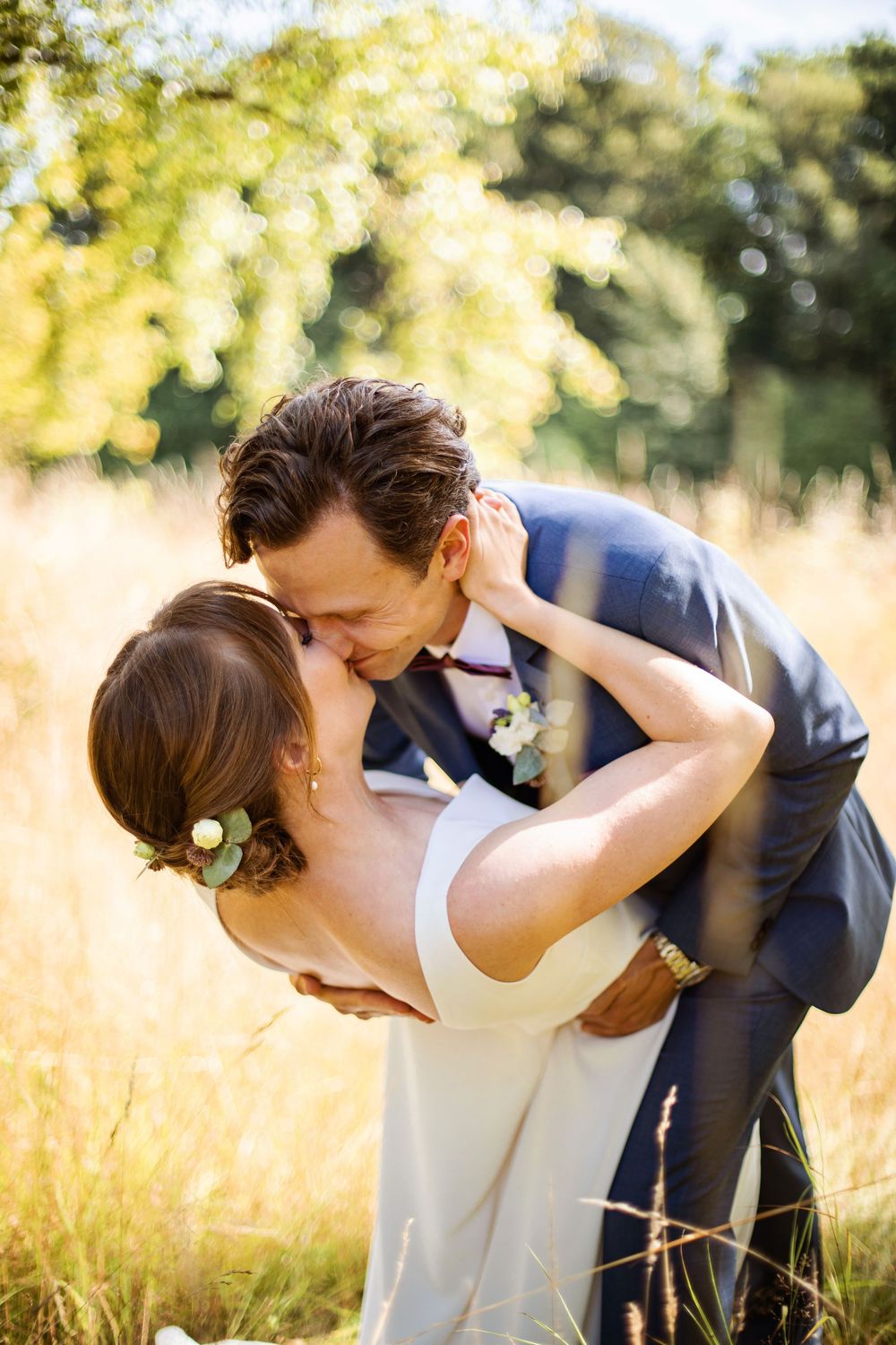 A bride and groom share a romantic kiss in a sunlit golden field, with the groom dipping his bride gently.
