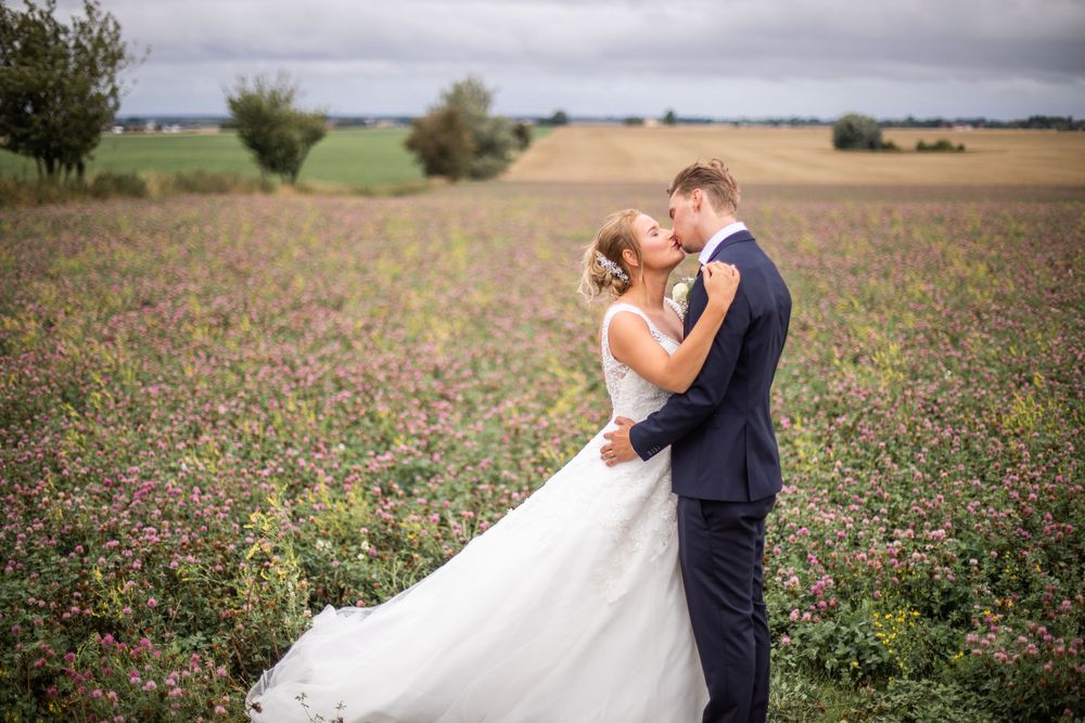 Bride and groom kissing in a blooming purple flower field on their wedding day.