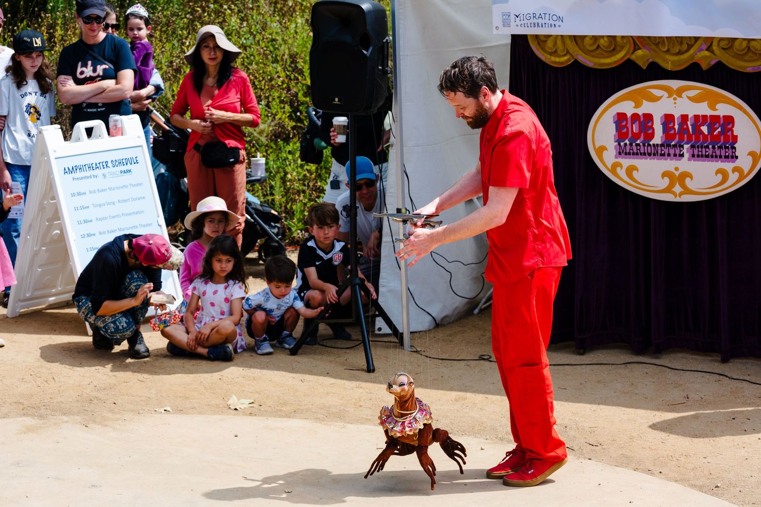 An event photo of a Bob Baker puppeteering a seal puppet in a red outfit in front of a crowd at the friends of ballona migration event.