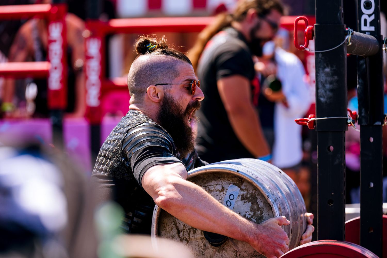 A bearded man competes at Santa Monica's Strongest Strongman competition. He is attempting to complete keg carry by lifting it over the bar