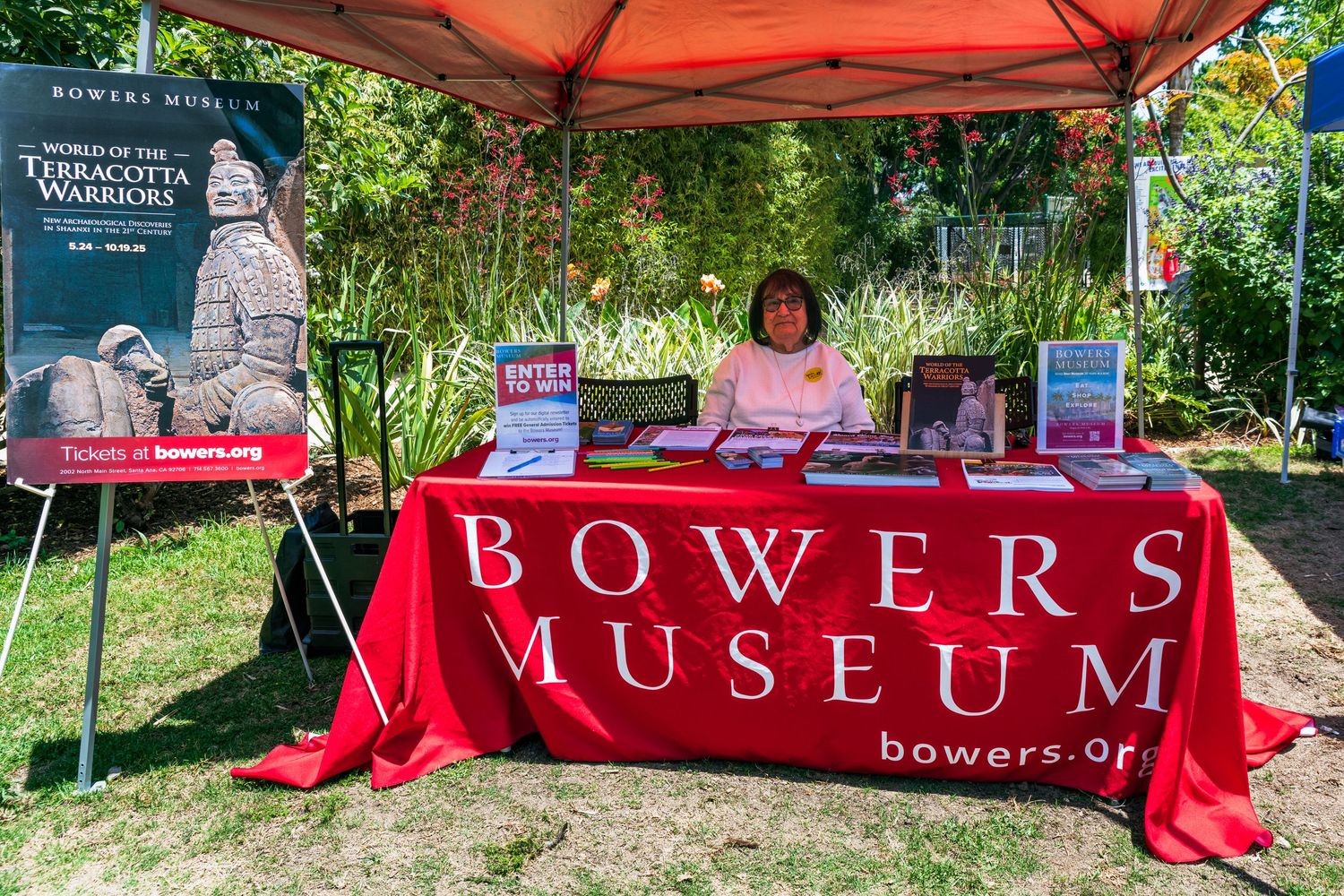 A photo of the Bowers Museum booth space at the party for the planet event at the Santa Ana zoo. A lady in a pink dress sits at the table.
