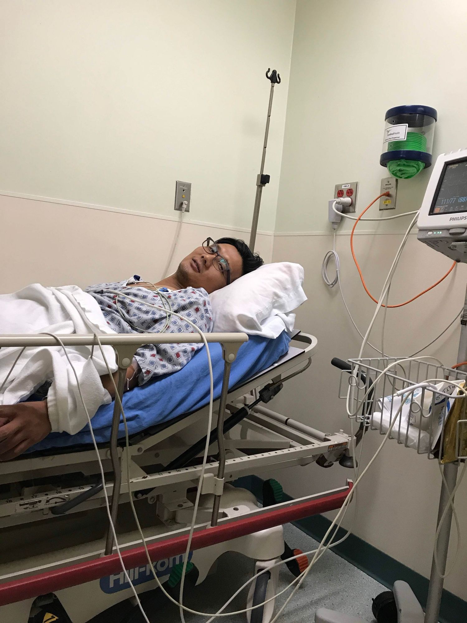 Patient resting in hospital bed connected to medical monitors and IV lines in a clinical setting.