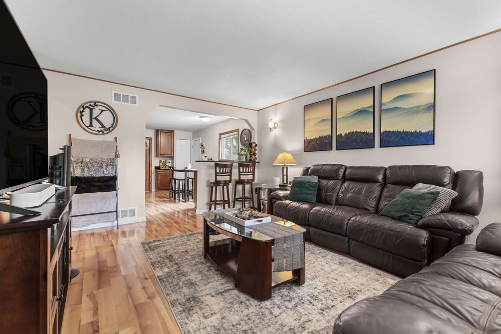 Spacious living room with dark leather reclining sofa, hardwood floors, and open kitchen view.